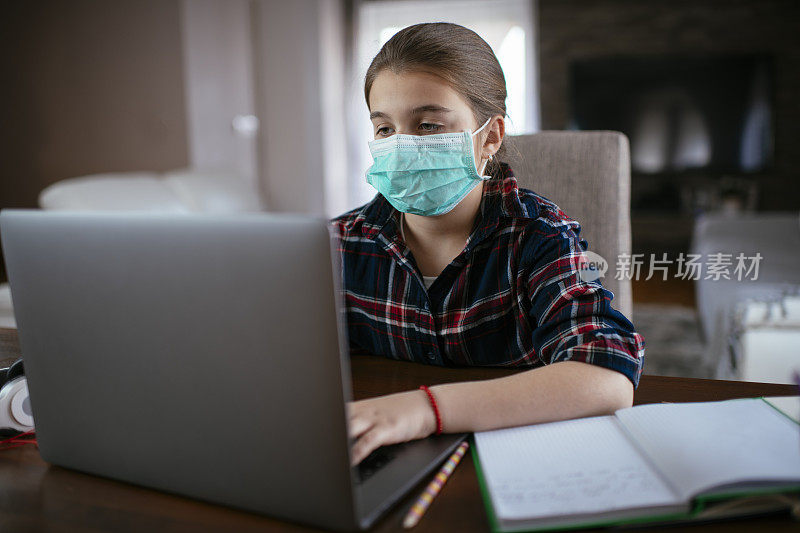 冠状病毒的爆发。封锁和学校关闭女学生戴着防护面具观看在线教育课。COVID-19大流行迫使儿童在线学习。股票辐透