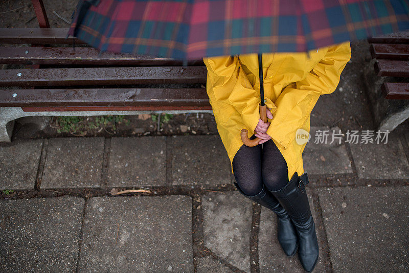 穿着黄色雨衣的年轻女子在公园里度过雨天