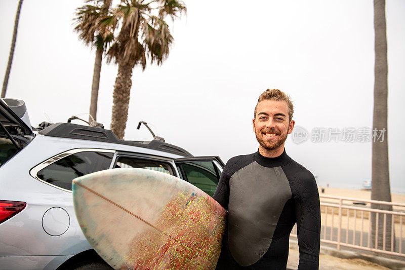 冲浪者拿着他的冲浪板站在汽车旁边