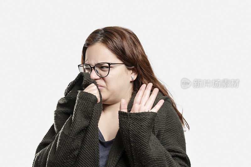 年轻女子用手捂住鼻子，表明灰色背景上有孤立的臭气