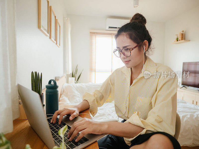 一位亚洲女性在家里开电话会议时使用笔记本电脑。