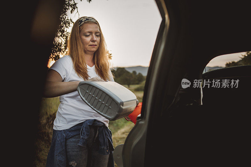 一位妇女在路上试图修理一辆坏了的汽车。这位妇女给她的车加油，试图继续旅程。一个女人带着一桶汽油在一辆车旁边