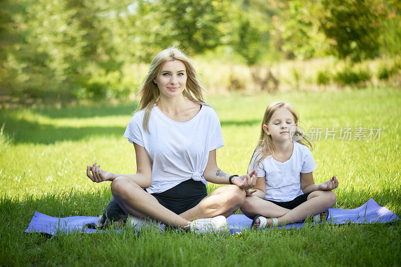 中年母亲练习瑜伽与蹒跚学步的女儿，美丽的母亲和女儿训练在一个夏天的一天户外。