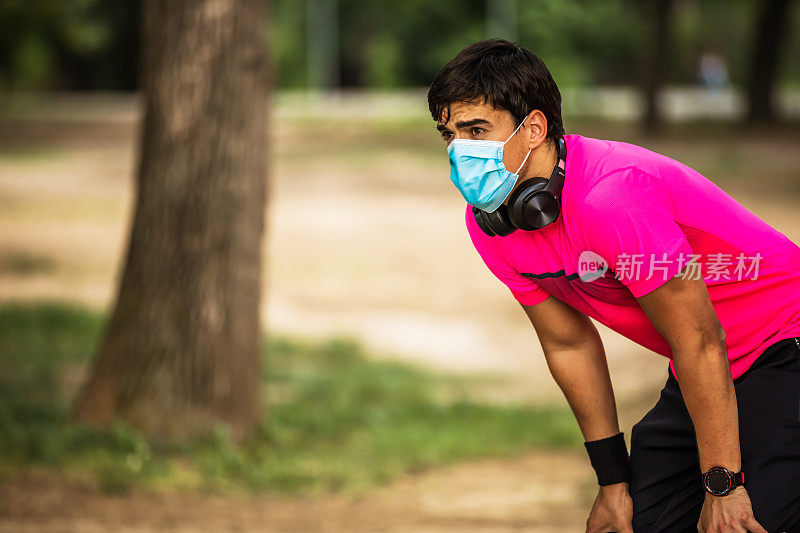 运动员戴医用口罩和耳机，在城市环境中锻炼，跑步。疲惫不堪的人用医用口罩奔跑。呼吸问题。