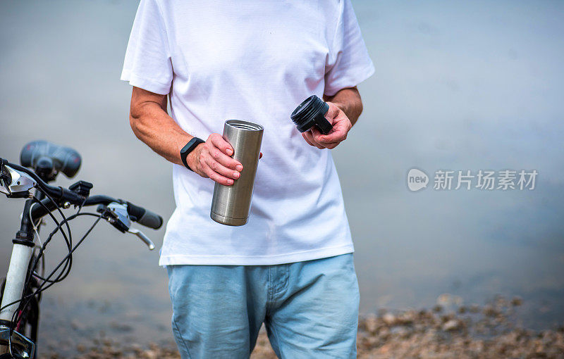 一名男子在湖边骑完自行车后拿着水瓶休息