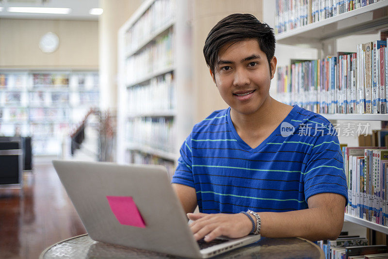 亚洲男人学生微笑和使用笔记本电脑做作业在图书馆