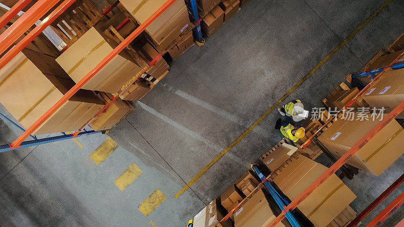 从上至下的视角:工人们站在零售仓库的货架上，用数码平板电脑和谈论包裹运送。员工在产品配送物流中心工作