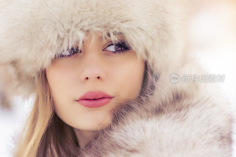 美丽的女子戴着皮帽在冬天的城市公园里，在白雪皑皑的天气里伴着飘落的雪花，特写