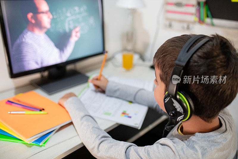 远程学习中，一个男孩戴着耳机坐在家里的桌子旁。理念线上教育、家庭教育、科技、学校