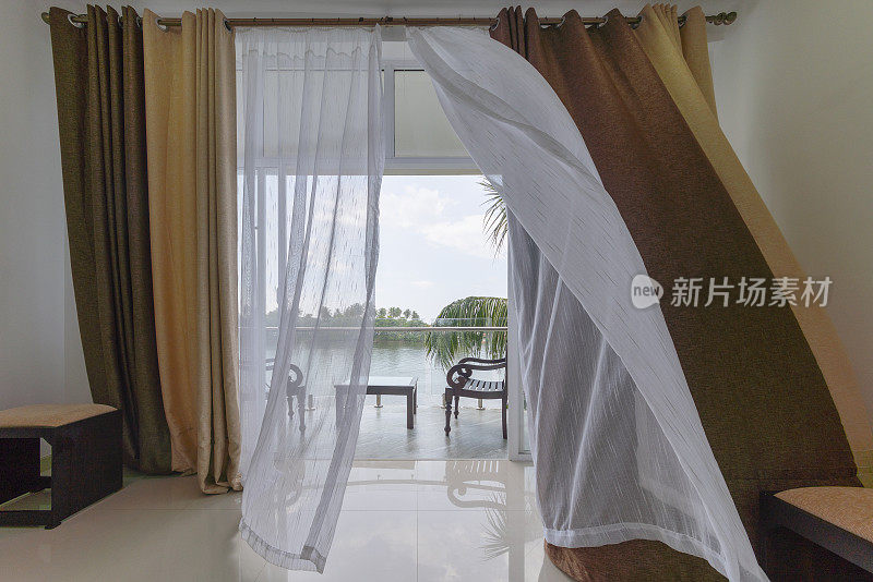 风吹动着敞开的阳台窗户上的窗帘，从现代化的空酒店房间可以看到河上的风景。