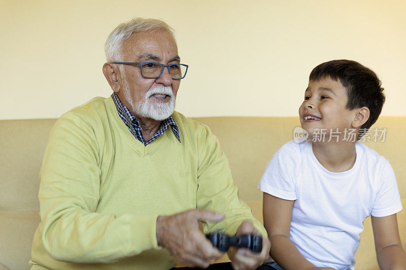 爷爷和孙子在家里玩电子游戏。的时间和家人在一起。