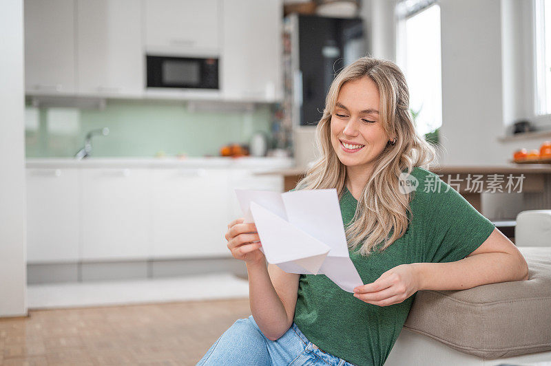 年轻女子微笑着在家里读一封信