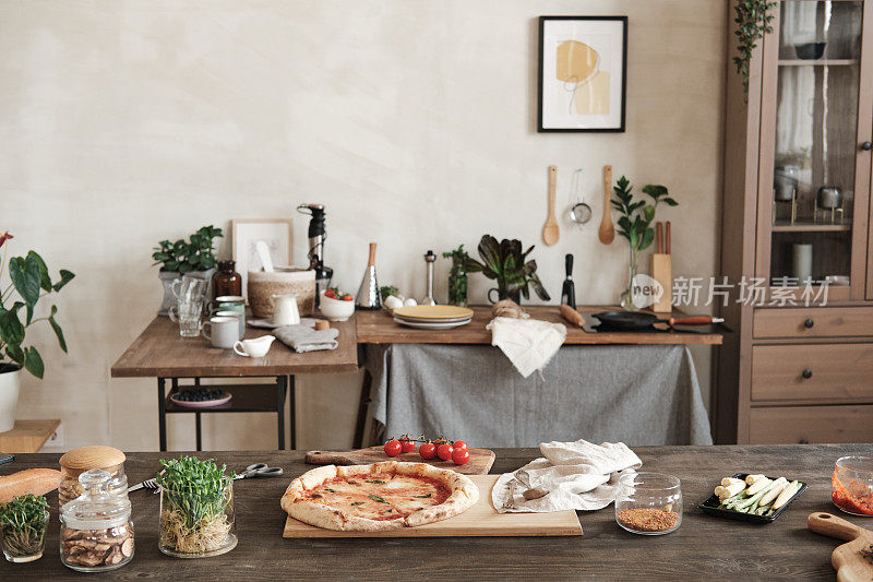 准备好的披萨放在木板上，桌子上有配料和香料罐，桌子的背景是器皿和陶器
