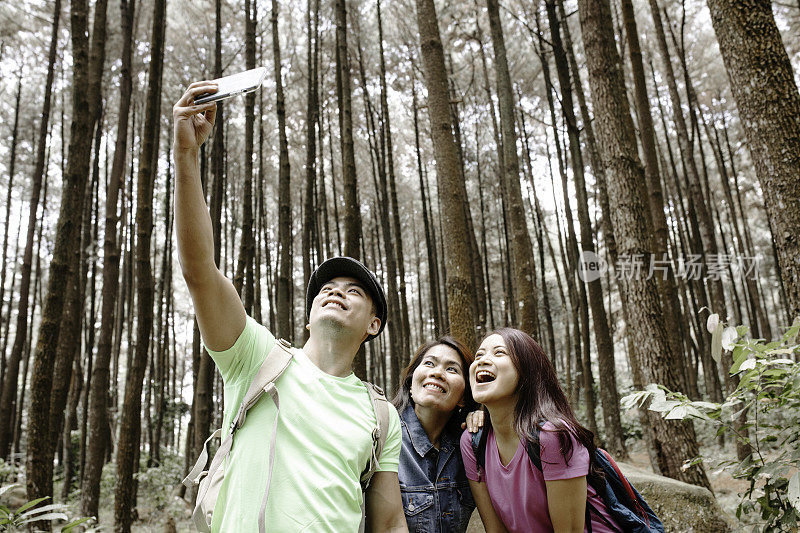 三个亚洲朋友在森林里散步时用智能手机自拍
