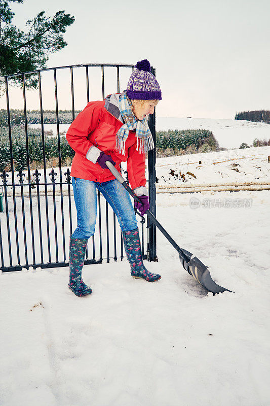 一位年长的妇女正在用雪铲清理前院的雪