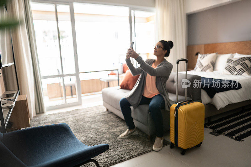 酒店房间里的女人用智能手机拍照或视频通话