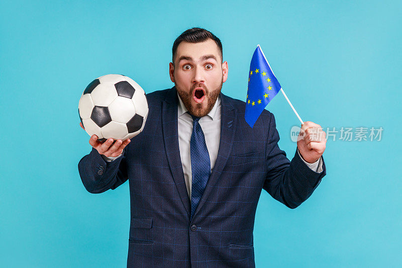 非常惊讶的男人穿着深色的西装，手里拿着欧盟的旗帜和足球，支持最喜欢的球队获得冠军。