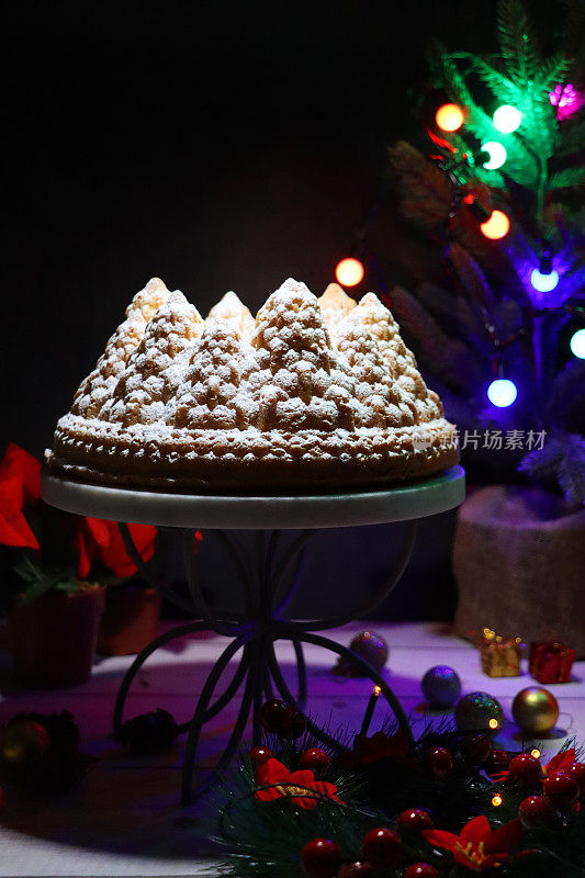 自制的形象，圣诞树形状，白色的柠檬毛绒绒的Bundt蛋糕，大理石和金属蛋糕架周围的圣诞装饰，柠檬味的环海绵覆盖着糖霜，明亮的童话灯，黑色背景