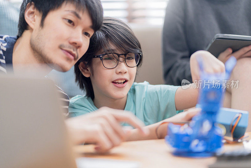 在家学习理念，亚洲男孩和父母成功控制机器人手臂在数码平板电脑和电脑键盘上，快乐的家庭在家里学习编程控制机器人