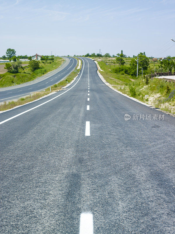 柏油路在绿色的田野上蓝色的多云的天空背景