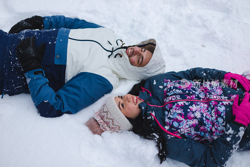 这是一对年轻美丽浪漫的夫妇躺在雪地里的照片，他们穿着色彩鲜艳的衣服