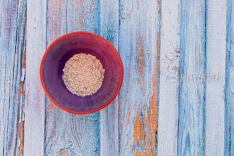 燕麦片在一个紫色陶瓷碗在一个蓝色质朴的木制背景与复制空间的右侧