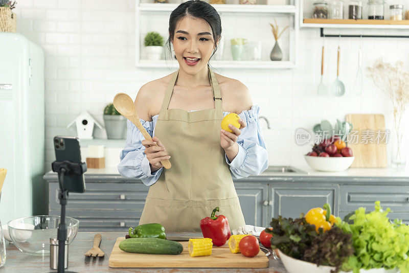 亚洲女性美食博主在智能手机摄像头前烹饪沙拉，同时在家里的厨房录制vlog视频和直播。