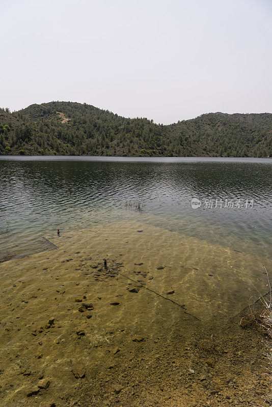 低角广角拍摄的淹没在湖边的混凝土板与对岸的森林山脉