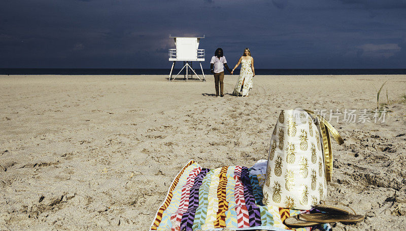 一对情侣留下毛巾和沙滩包，手牵着手走在田园诗般的海滩上
