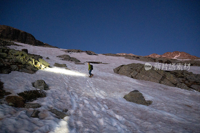 黎明时分，女登山者沿着雪道攀登山顶