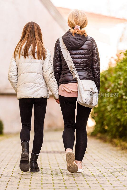 后视图的母亲和女儿在冬天一起走在城镇街道