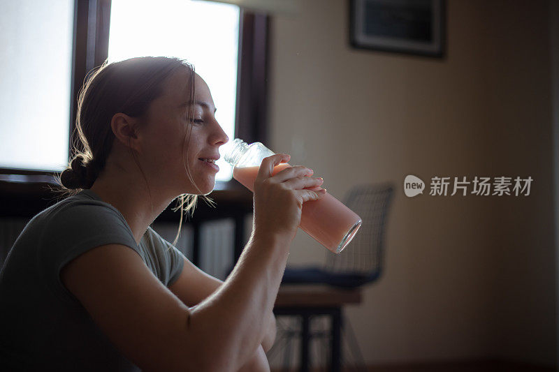 年轻女子在家里的客厅锻炼期间补水。