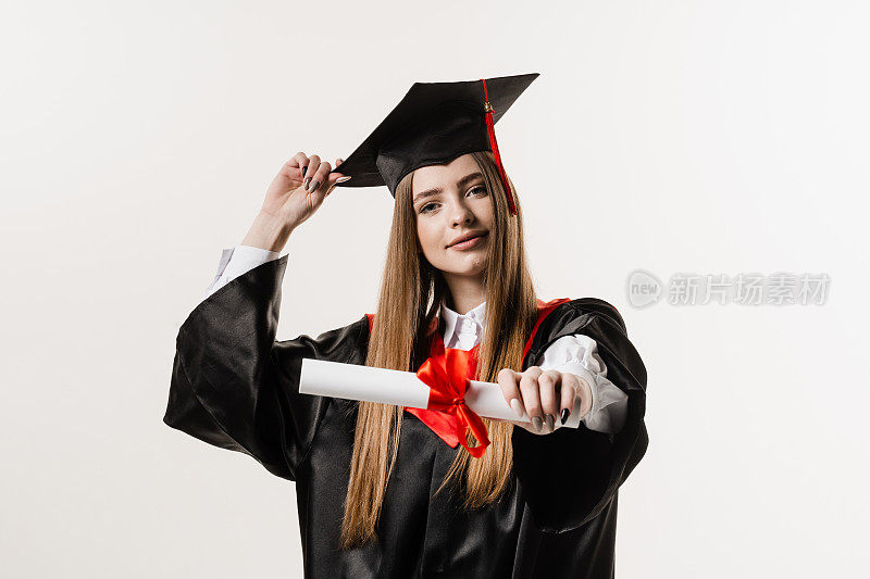 身着白底黑毕业服的女研究生手中拿着红丝带的硕士学位证书。毕业女孩高中毕业，庆祝学业成就。