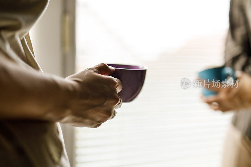 两个年轻女人站在窗边，喝着咖啡聊天