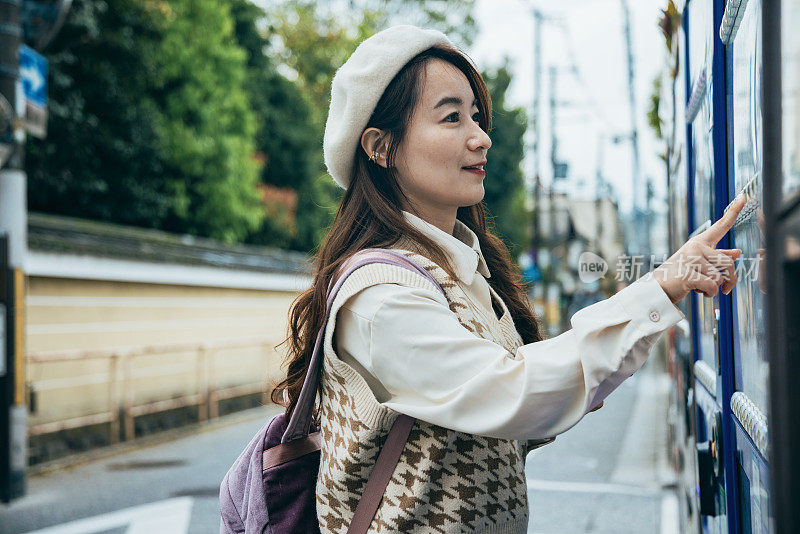 在日本京都街头，一名亚洲妇女正在自动售货机购买商品。