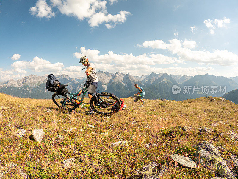 一对夫妇在瑞士阿尔卑斯山骑自行车，日落时分在山顶搭起帐篷