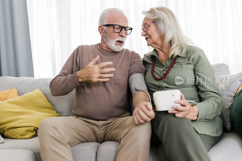 老夫妇在家测血压。妻子正在用血压计检查丈夫手臂上的血压