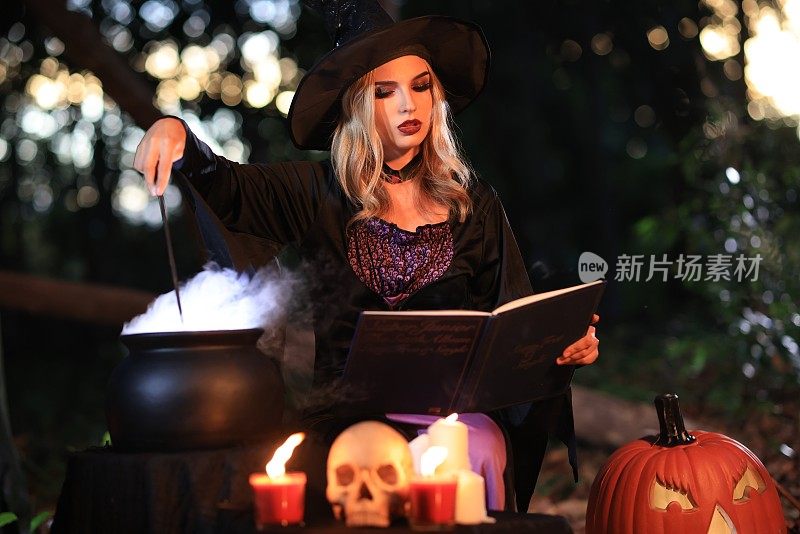 幻想中的女女巫会变魔术，手里拿着一根魔杖和一本魔法书，念着从沸腾的大桶里冒出来的白魔法烟。万圣节的主题。女巫在万圣节那天举行仪式