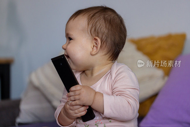 可爱的白人女婴坐在床上玩电视遥控器