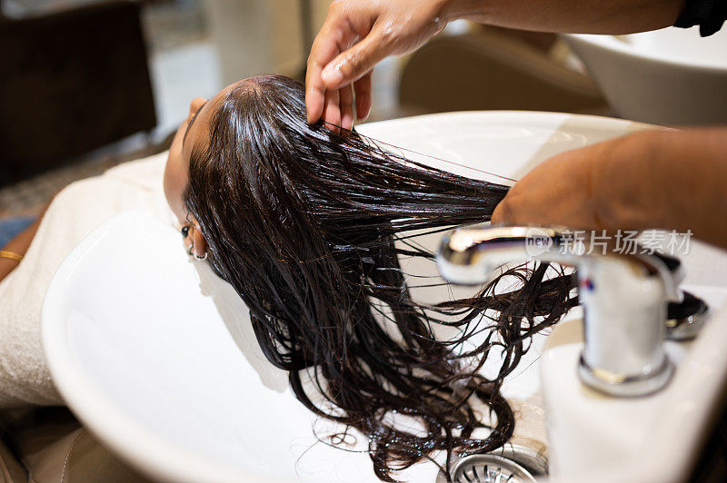 年轻女子一边享受着专业理发师给她洗头的乐趣
