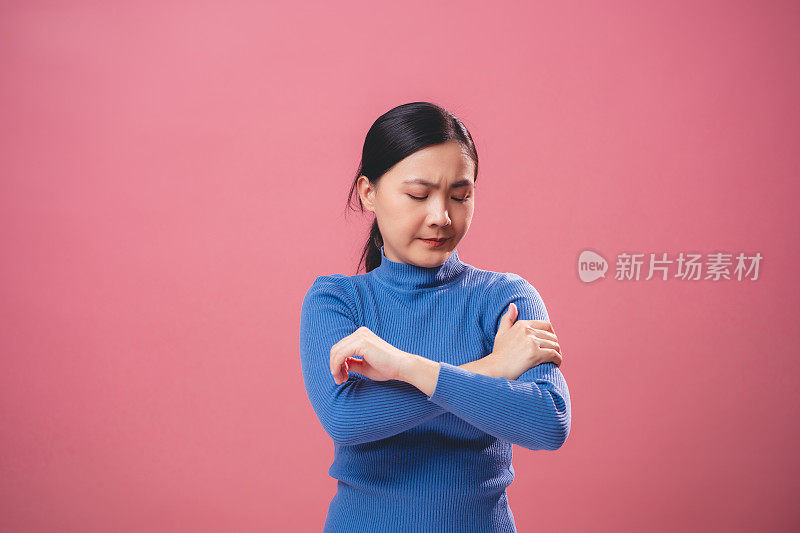患有手臂疼痛的亚洲妇女孤立地站在粉红色的背景上。