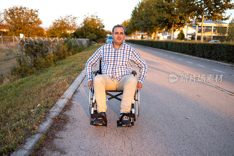 残疾白人中年男子的肖像，推着轮椅，在附近的人行道上