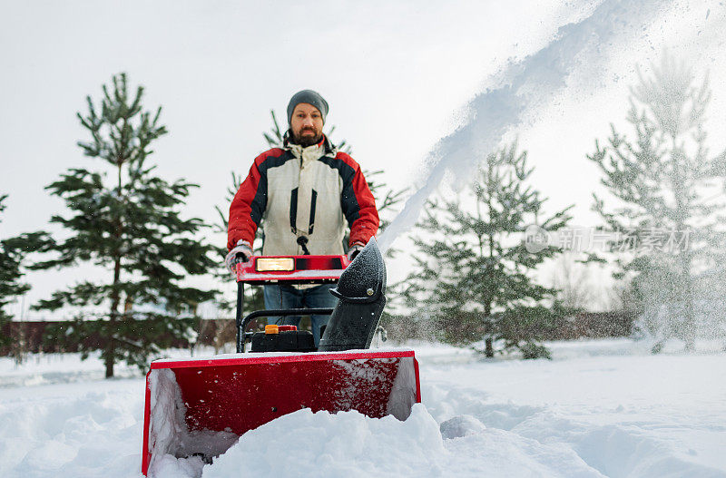 一名成年男子在大雪中用吹雪机除雪