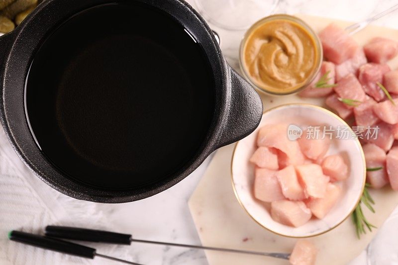 火锅锅用油，叉子和生肉块放在白色大理石桌上，平铺