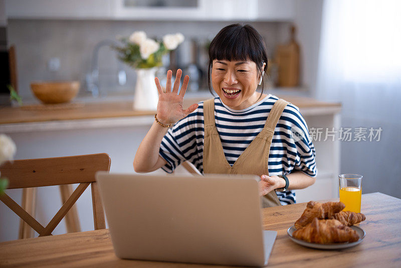 一个亚洲女人一边用笔记本电脑打字一边吃早餐