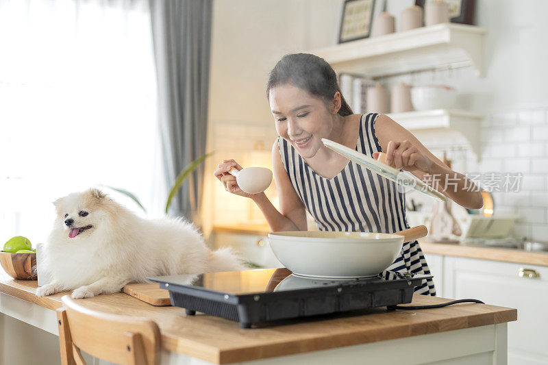 新鲜微笑的亚洲青少年女性烹饪会议与她的波美拉尼犬白色膝上狗在厨房与幸福好氛围的女人烹饪，而宠物她的狗在厨房家庭内部