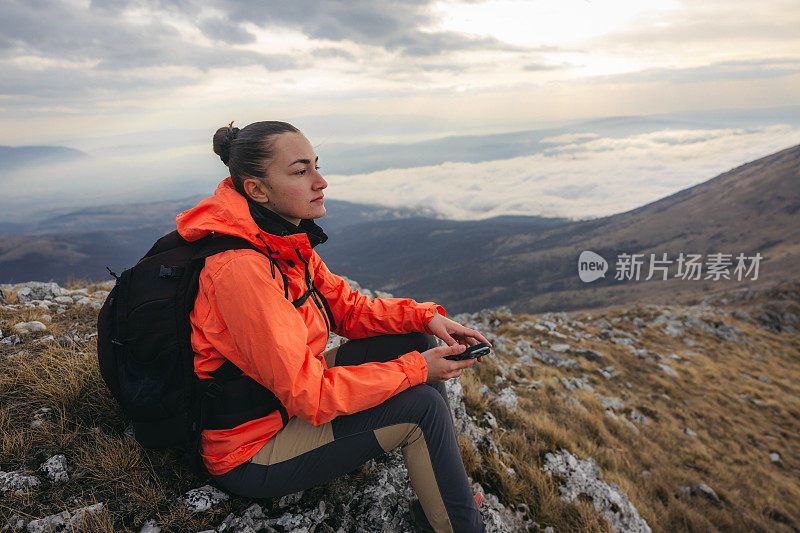 美丽的女徒步旅行者坐在山顶的岩石上