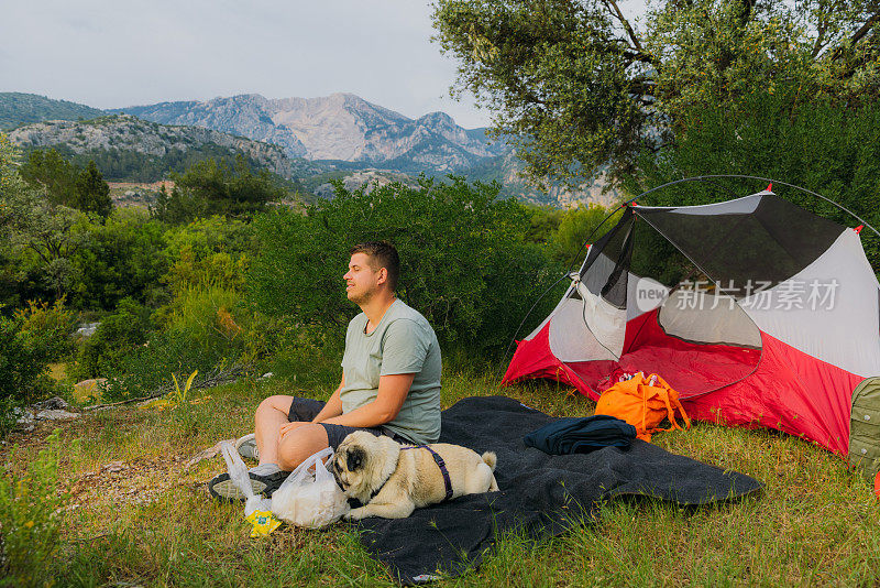 快乐的男人带着狗在土耳其俯瞰日落露营