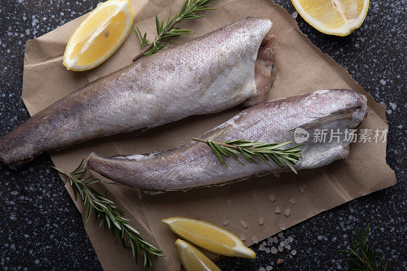 新鲜的生鱼点缀着柠檬和迷迭香，呈现在黑暗，纹理背景，完美的烹饪主题和美食烹饪内容。