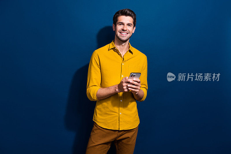 英俊的年轻人的照片肖像手持设备电子商务阅读帖子穿着时尚的黄色服装孤立在深蓝色的背景